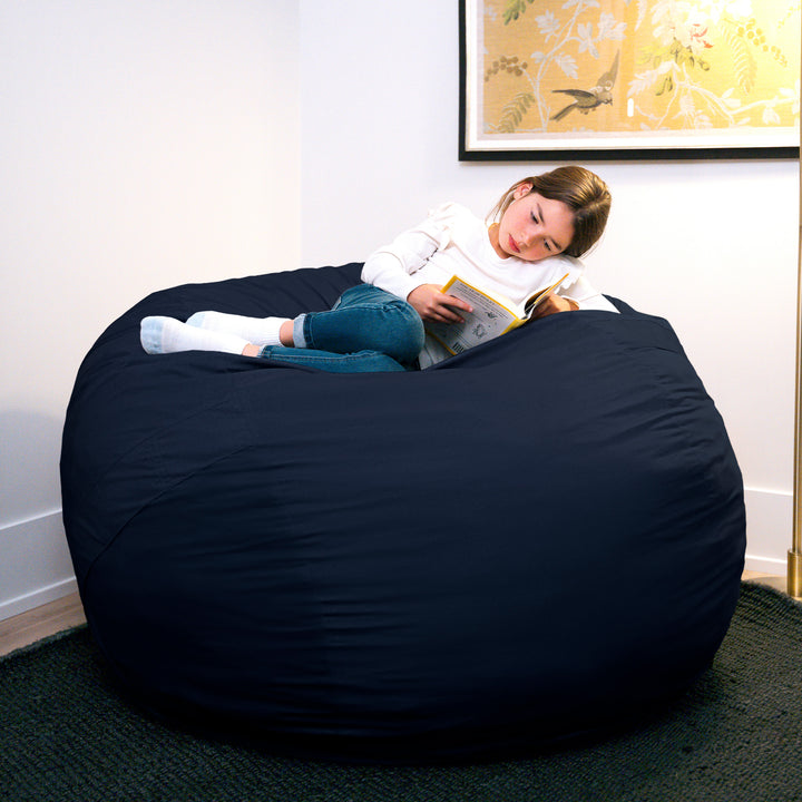 Person reading a book on a large navy bean bag chair in a room with a painting on the wall. #color_cobalt-brushed-denim