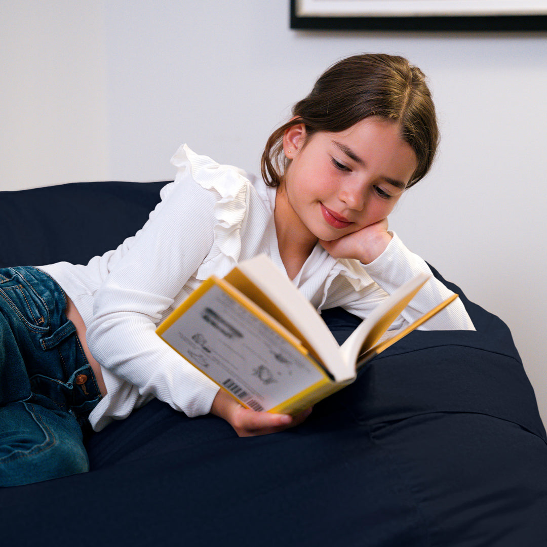Woman reading a book on a beanbag in a cozy living room. #color_cobalt-brushed-denim