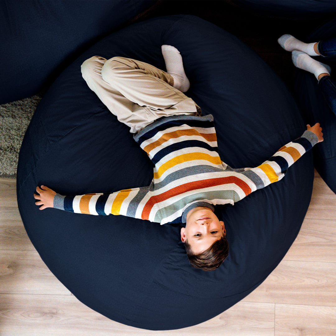 Child lying on a navy bean bag chair wearing a striped sweater. #color_cobalt-brushed-denim