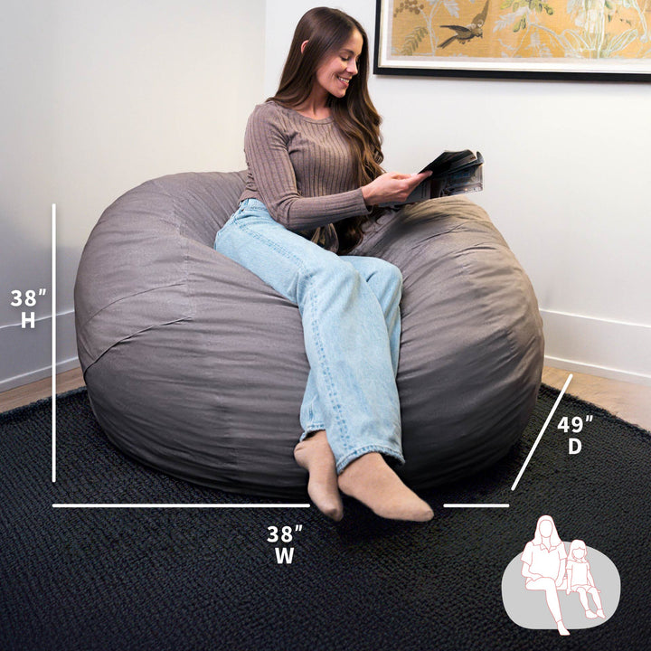 Woman sitting on a large gray bean bag chair with measurements displayed. #color_fog-brushed-denim