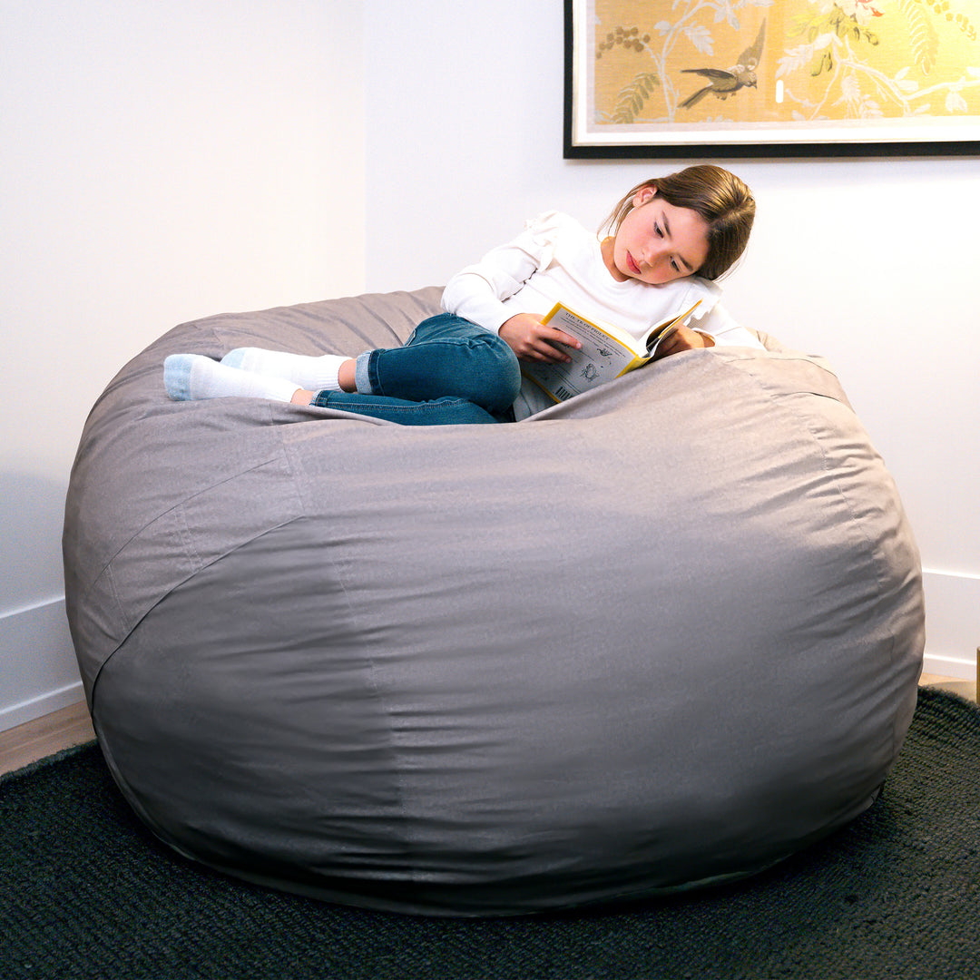 Person sitting on a large gray bean bag reading a book in a room with a framed picture on the wall. #color_fog-brushed-denim