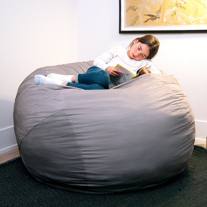 Person sitting on a large gray bean bag reading a book in a room with a framed picture on the wall. #color_fog-brushed-denim