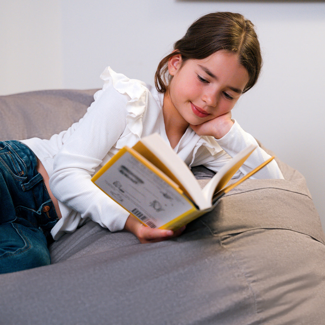 Young girl reading a book on a beanbag #color_fog-brushed-denim