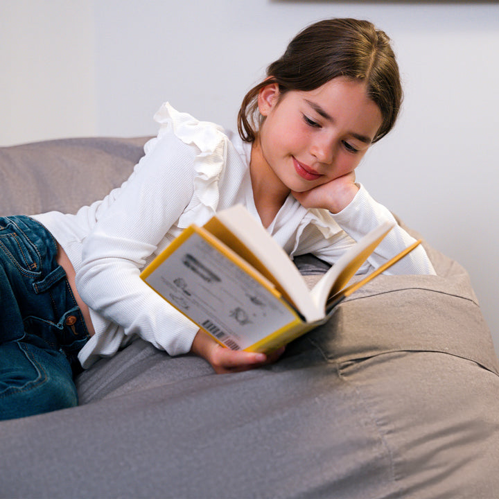 Young girl reading a book on a beanbag #color_fog-brushed-denim