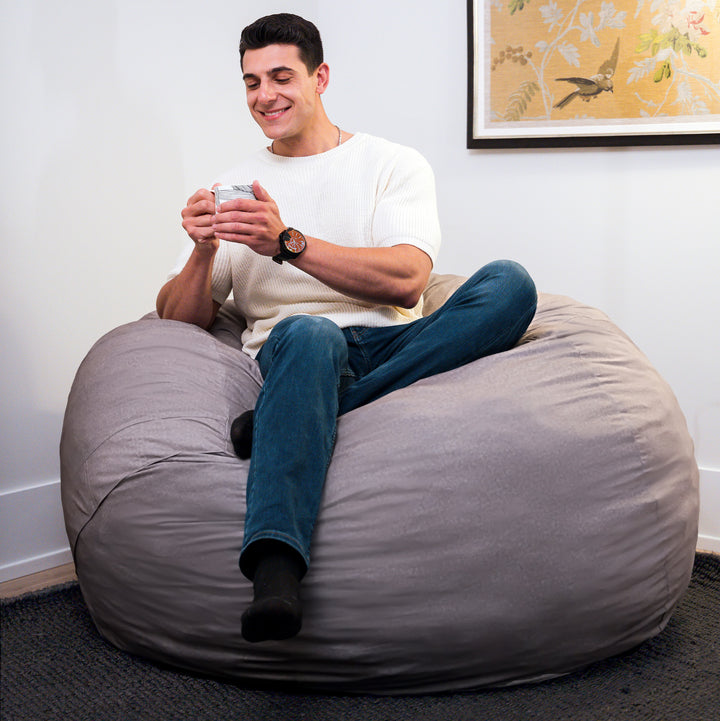 Man sitting on a large gray bean bag chair holding a phone, with a framed picture on the wall behind him. #color_fog-brushed-denim