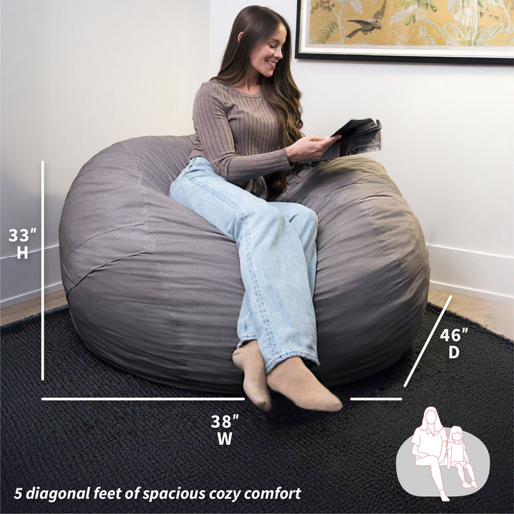 Woman sitting on a large gray bean bag chair with dimensions displayed. #color_fog-brushed-denim