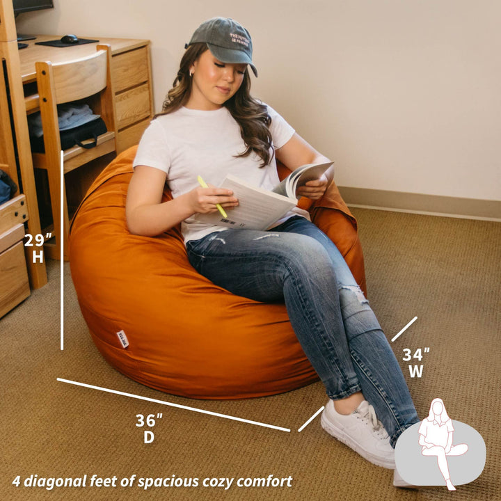 Person sitting on a large orange bean bag chair in a room with measurements displayed. #color_burnt-orange-brushed-denim