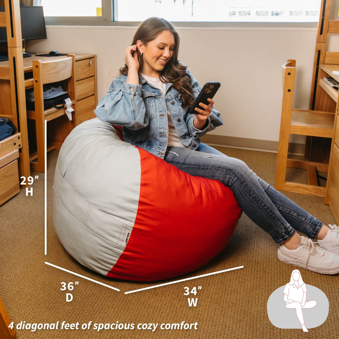 Person sitting on a red and gray bean bag chair in a room with desks and chairs. #color_scarlet-grey-brushed-denim
