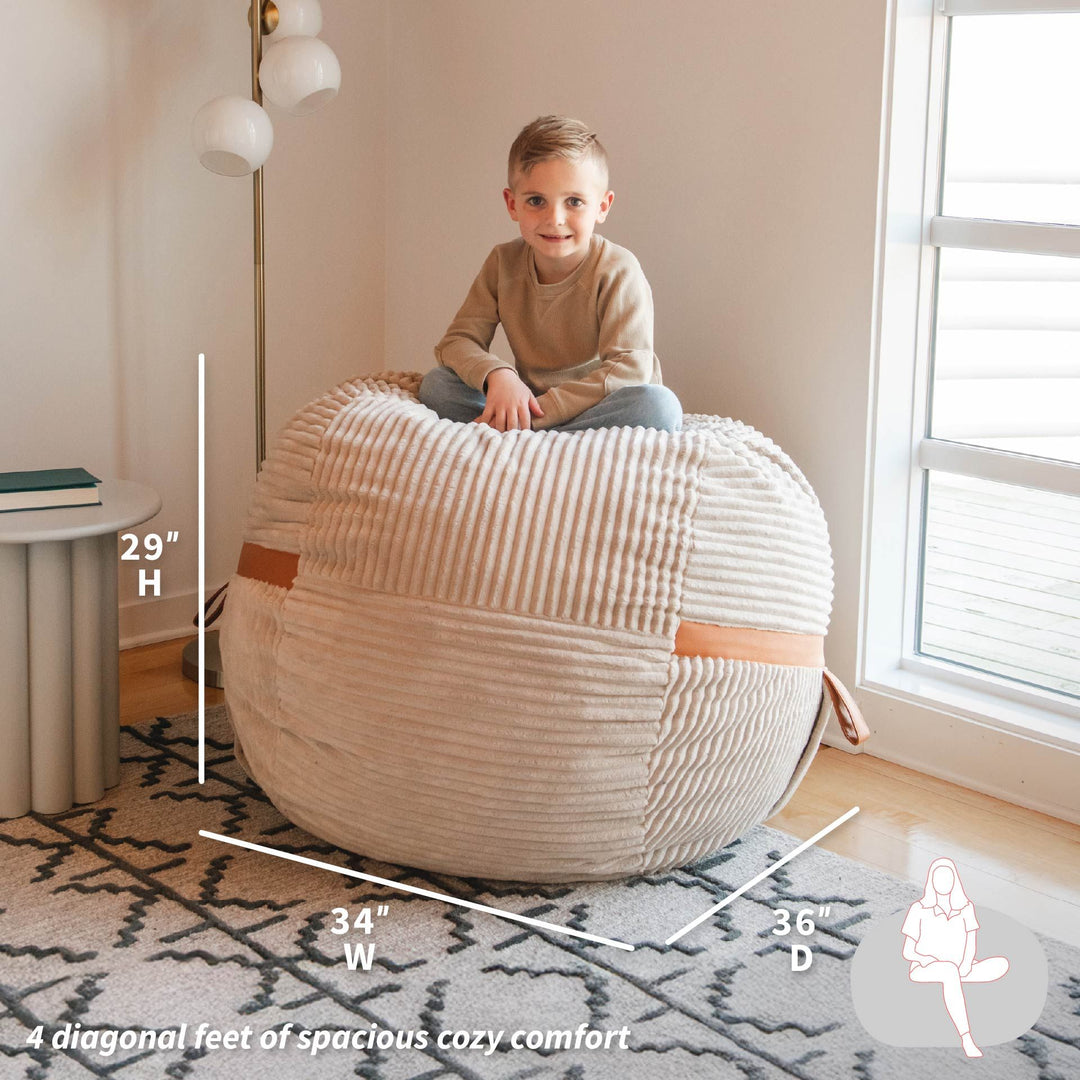 Child sitting on a textured ottoman with dimensions displayed, in a room setting. #color_vanilla-latte-corded-plush
