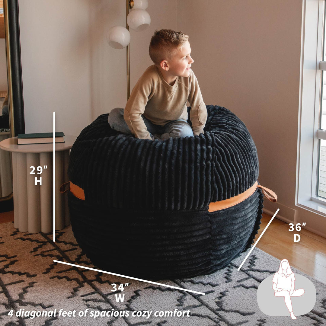 Child sitting on a large black textured ottoman with measurements indicated, in a home setting. #color_black-licorice-corded-plush