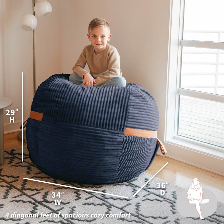 Child sitting on a navy bean bag chair with measurements indicated, in a room setting. #color_midnight-blue-corded-plush