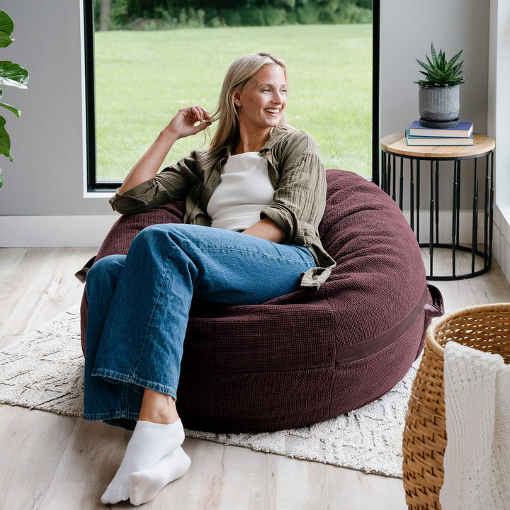 Woman sitting on a Merlot bean bag chair in a modern living room. #color_merlot-cloudweave