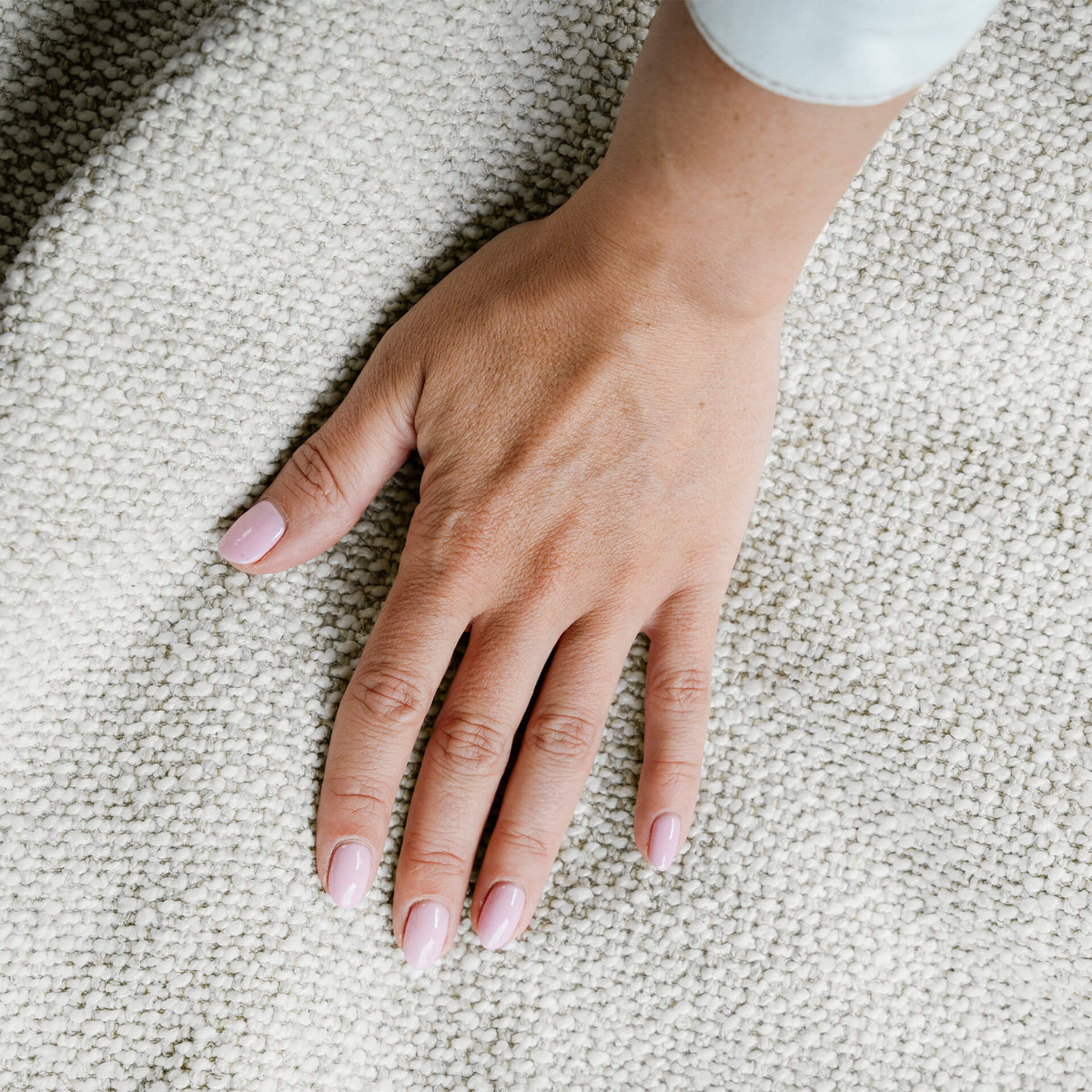 Hand with light pink nail polish on a textured beige surface 