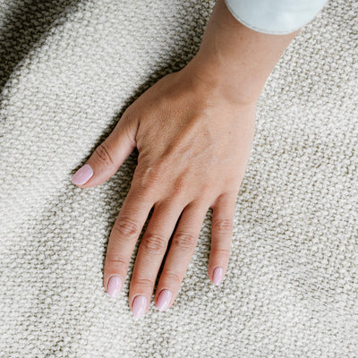 Hand with light pink nail polish on a textured beige surface 