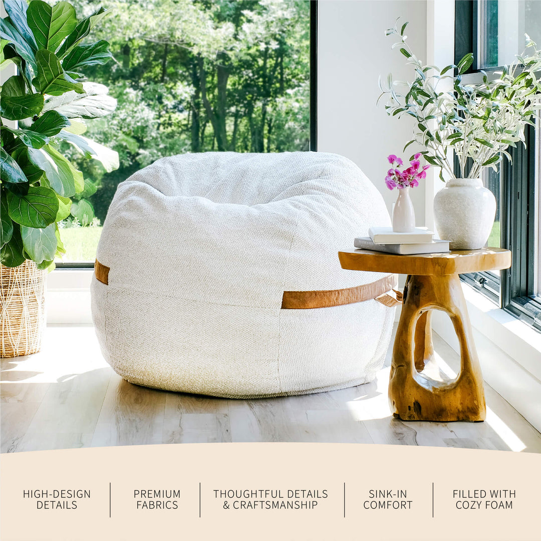 White bean bag chair in a bright room with a wooden side table and plants. #color_sandstone-textured-boucle