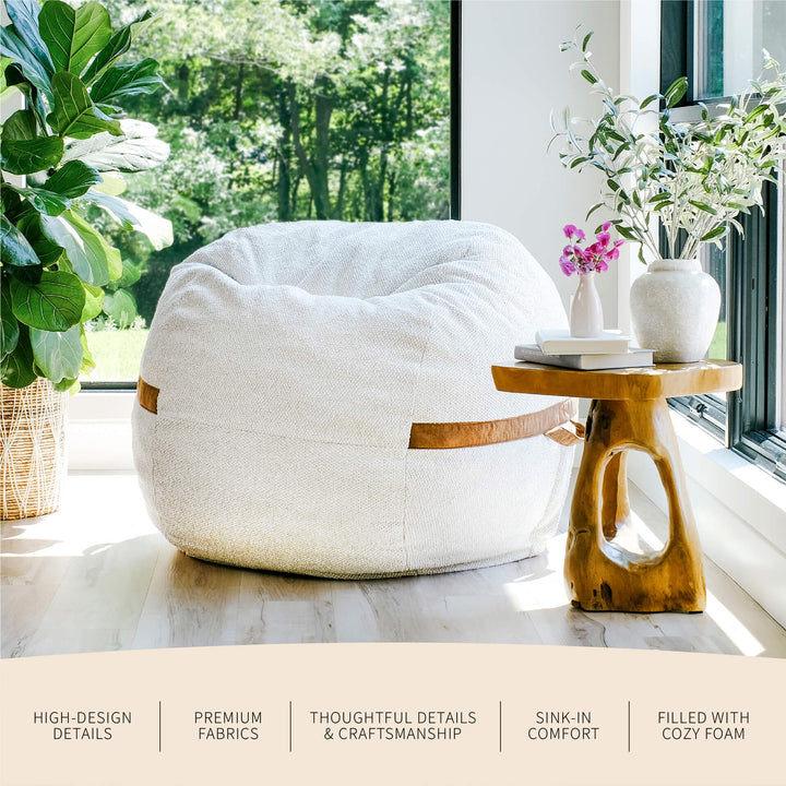 White bean bag chair in a bright room with a wooden side table and plants. #color_sandstone-textured-boucle