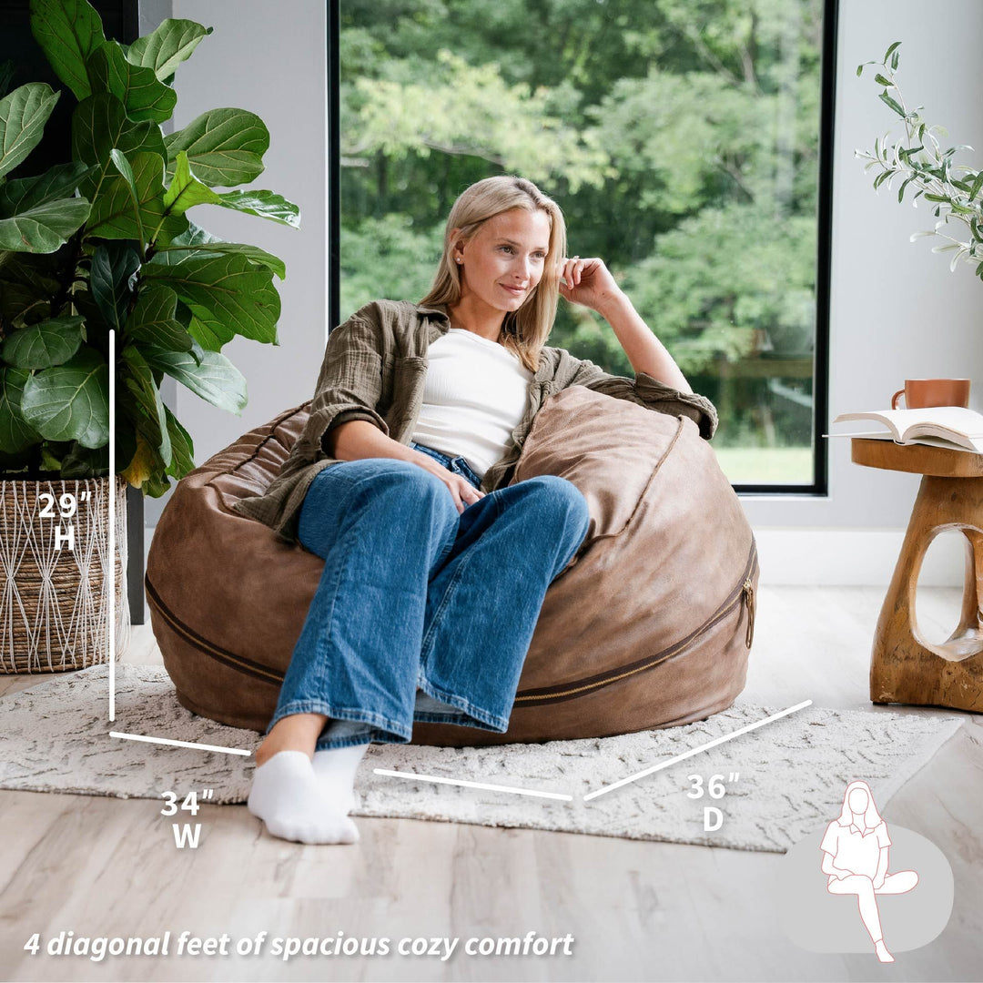 Woman sitting on a large brown bean bag chair in a room with plants and a window. #color_coffee-soft-vegan-leather