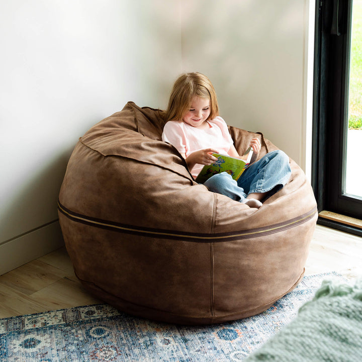 Child sitting in a large brown bean bag reading a book in a cozy room. #color_coffee-soft-vegan-leather