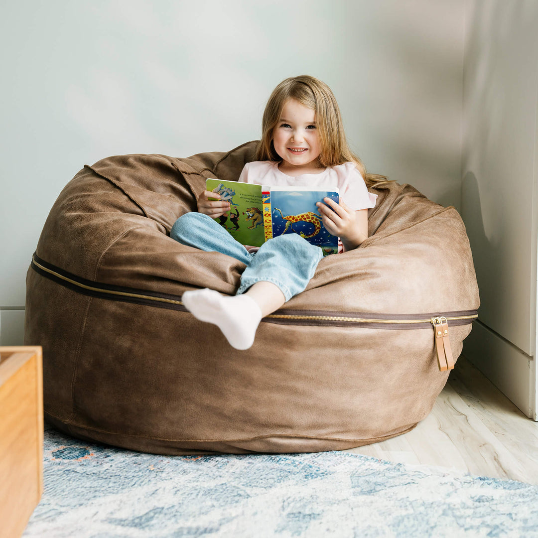 Child sitting on a brown bean bag reading a book in a cozy room. #color_coffee-soft-vegan-leather