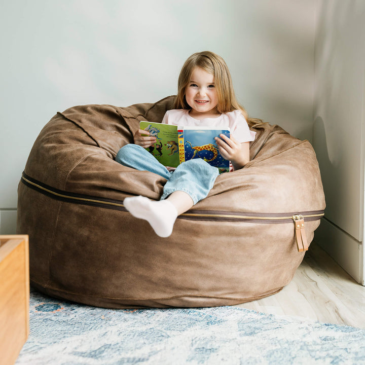 Child sitting on a brown bean bag reading a book in a cozy room. #color_coffee-soft-vegan-leather