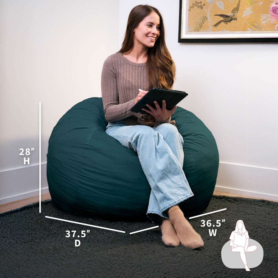 Woman sitting on a teal bean bag chair with dimensions displayed, holding a tablet.  #color_deep-sea-velveteen