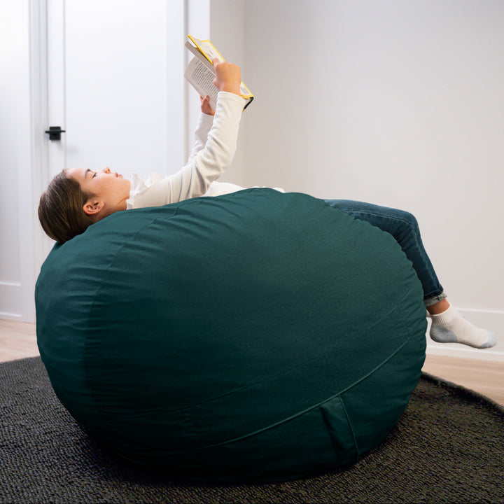 Person lying on a large teal bean bag reading a book in a room with white walls. #color_deep-sea-velveteen