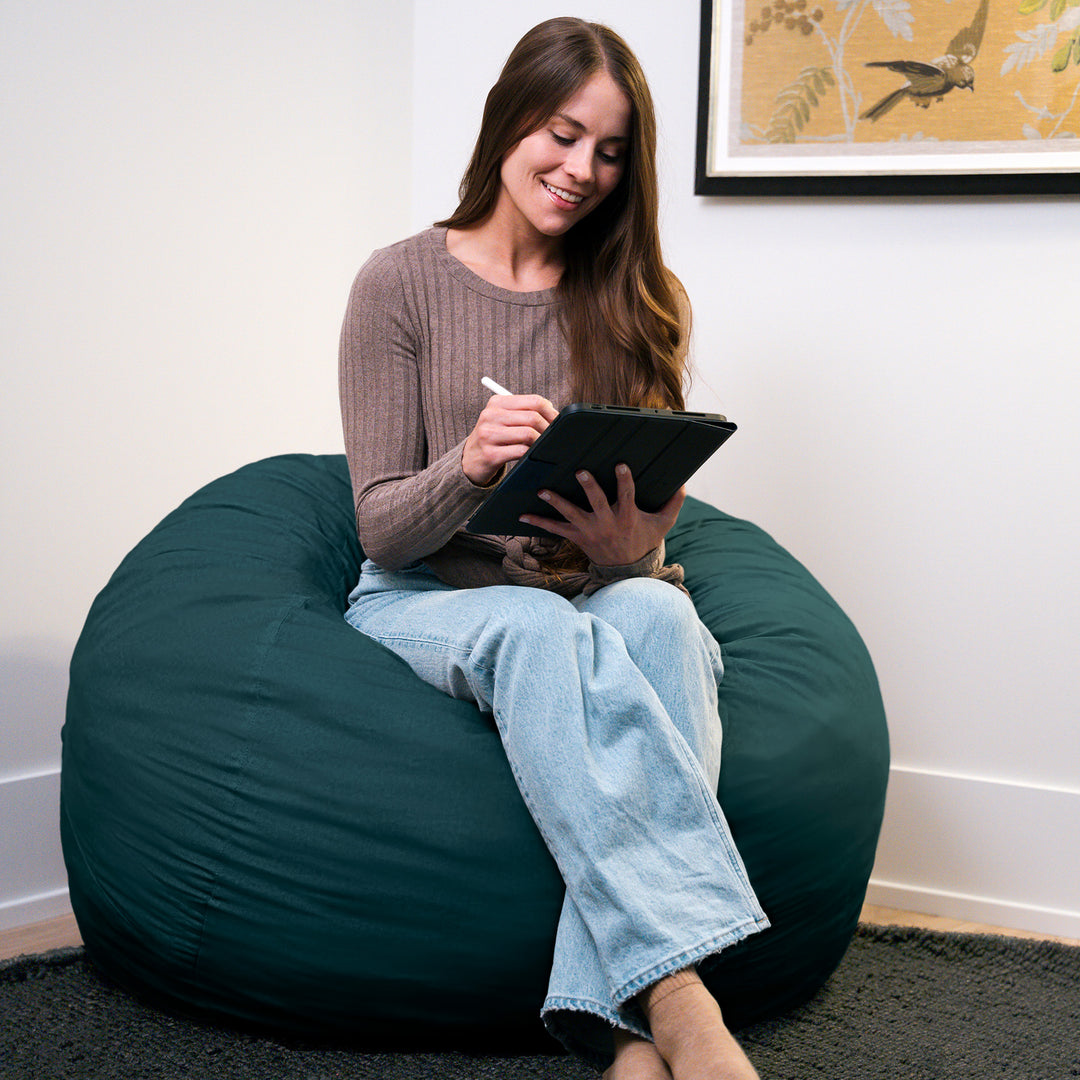 Woman sitting on a teal bean bag chair using a tablet. #color_deep-sea-velveteen