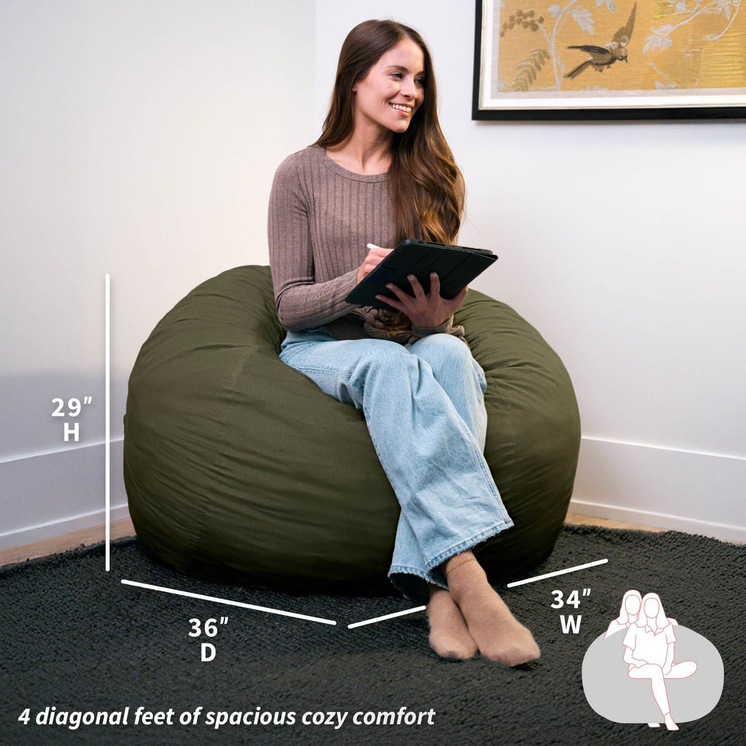 Woman sitting on a green bean bag chair with measurements displayed #color_forest-green-velveteen