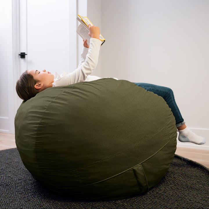 Person lying on a large green bean bag reading a book in a room. #color_forest-green-velveteen
