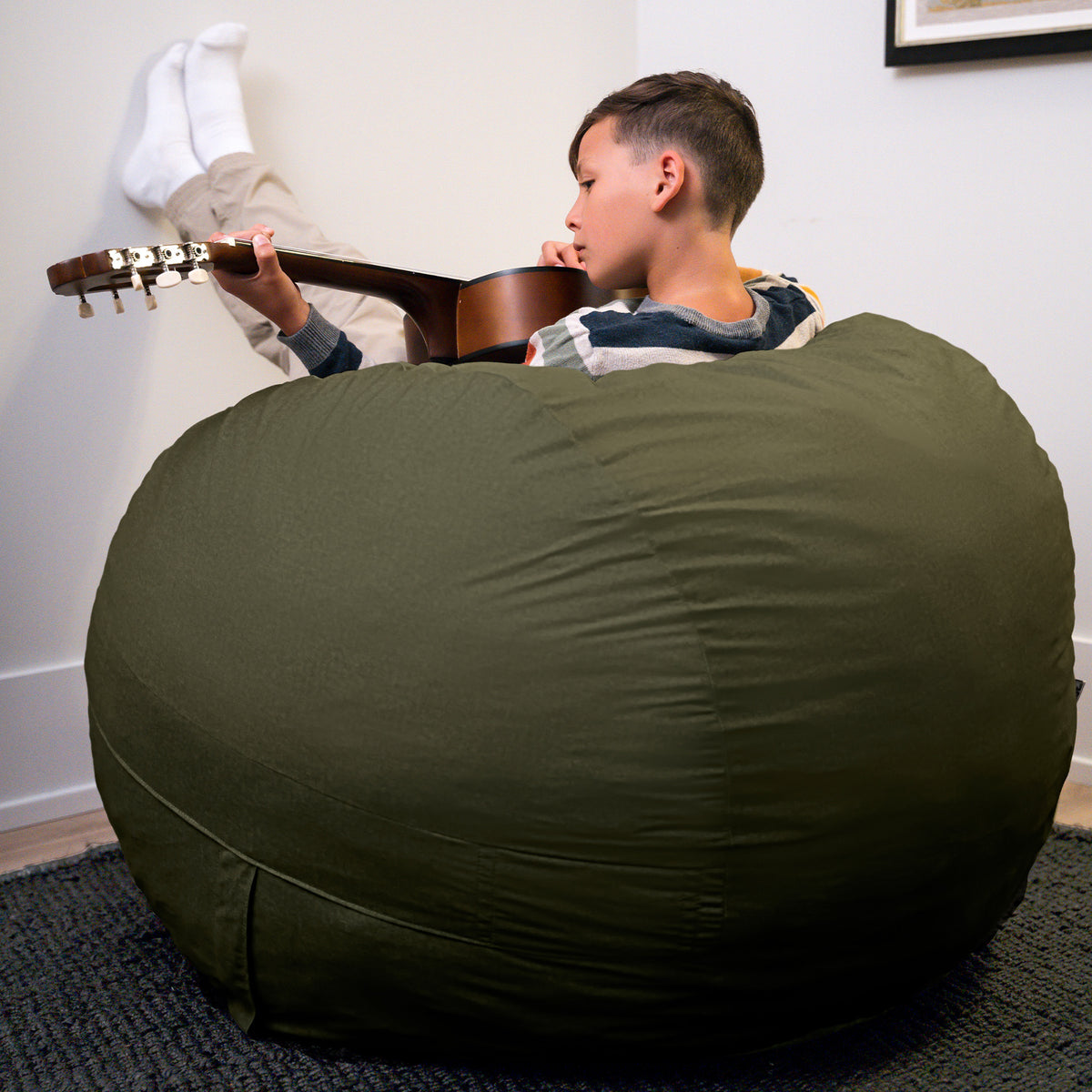 Person sitting on a large green bean bag holding a guitar in a casual indoor setting. 