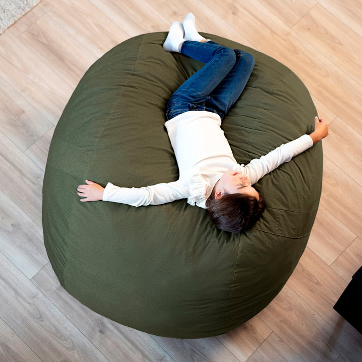 Person lying on a large green bean bag chair on a wooden floor #color_forest-green-velveteen