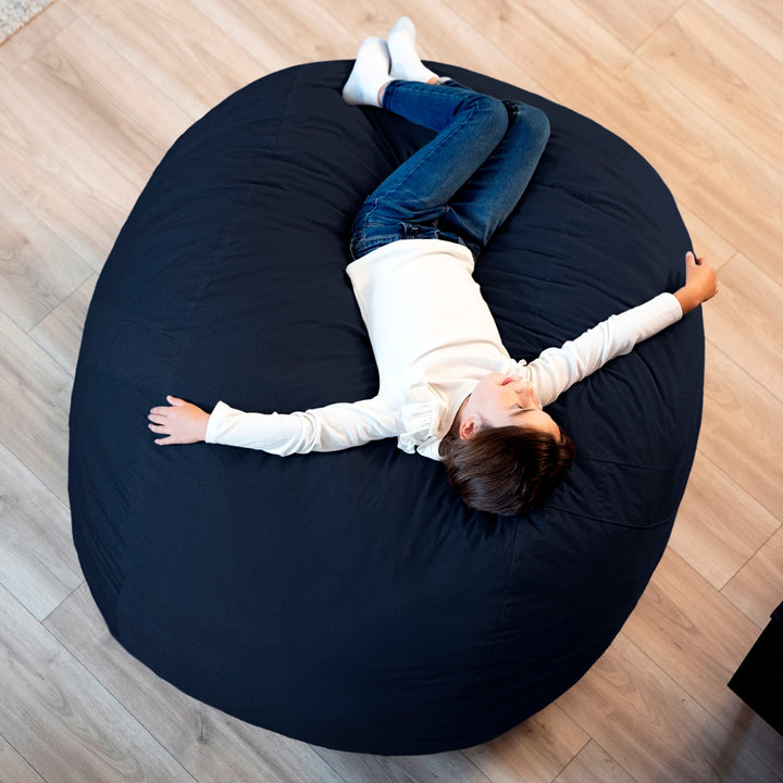 Person lying on a large black bean bag chair indoors. #color_cobalt-brushed-denim
