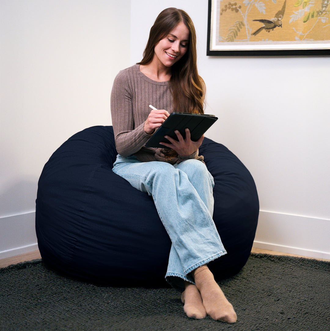 Woman sitting on a navy bean bag chair using a tablet. #color_cobalt-brushed-denim