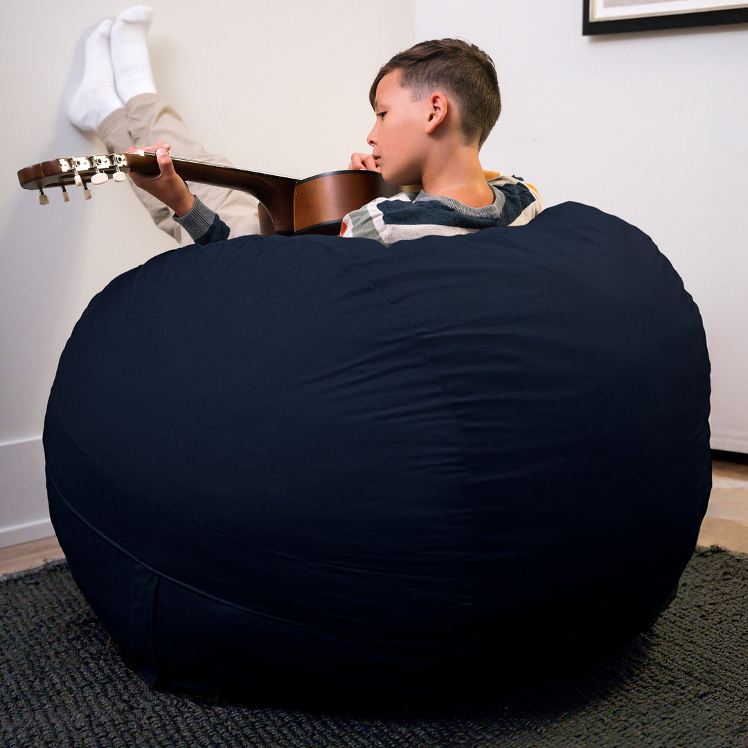 Child playing guitar on a large navy bean bag chair in a room. #color_cobalt-brushed-denim
