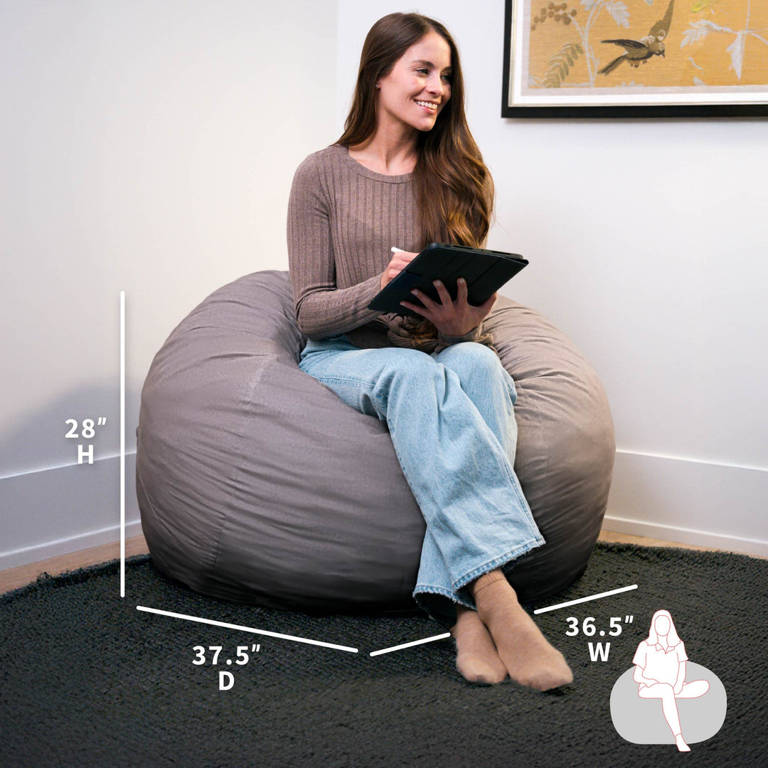 Woman sitting on a gray bean bag chair holding a tablet, with measurements displayed. #color_fog-brushed-denim