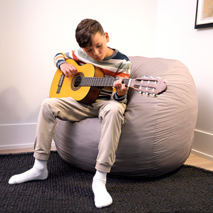 Child playing a guitar while sitting on a bean bag chair indoors. #color_fog-brushed-denim