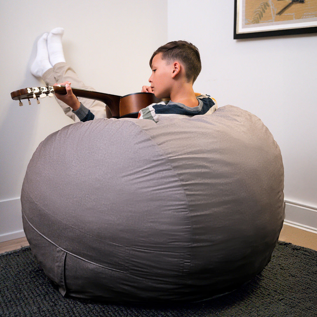 Child playing guitar next to a large gray bean bag chair in a room. #color_fog-brushed-denim