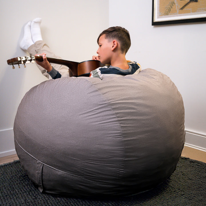 Child playing guitar next to a large gray bean bag chair in a room. #color_fog-brushed-denim