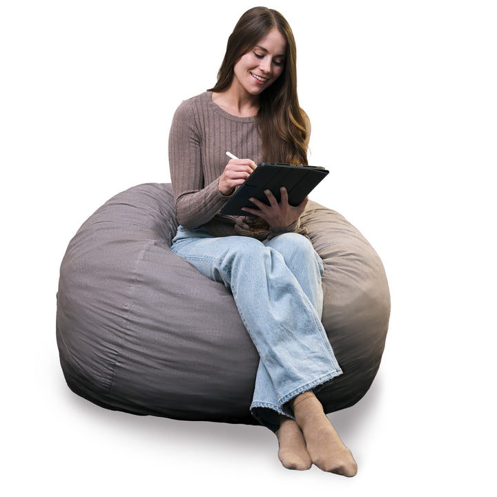 Woman sitting on a large gray bean bag chair using a tablet. #color_fog-brushed-denim