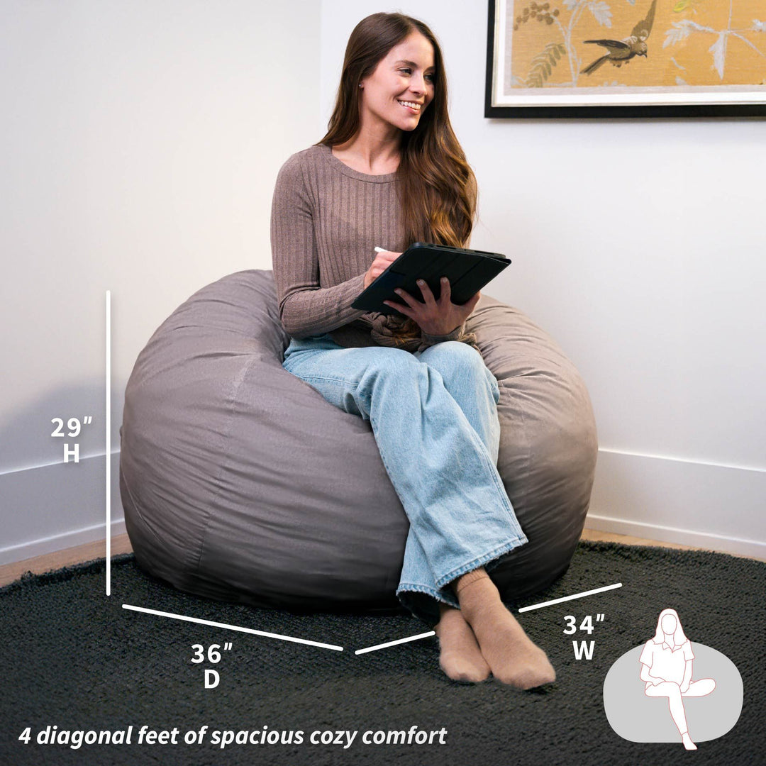 Woman sitting on a large gray bean bag chair with measurements displayed. #color_fog-brushed-denim