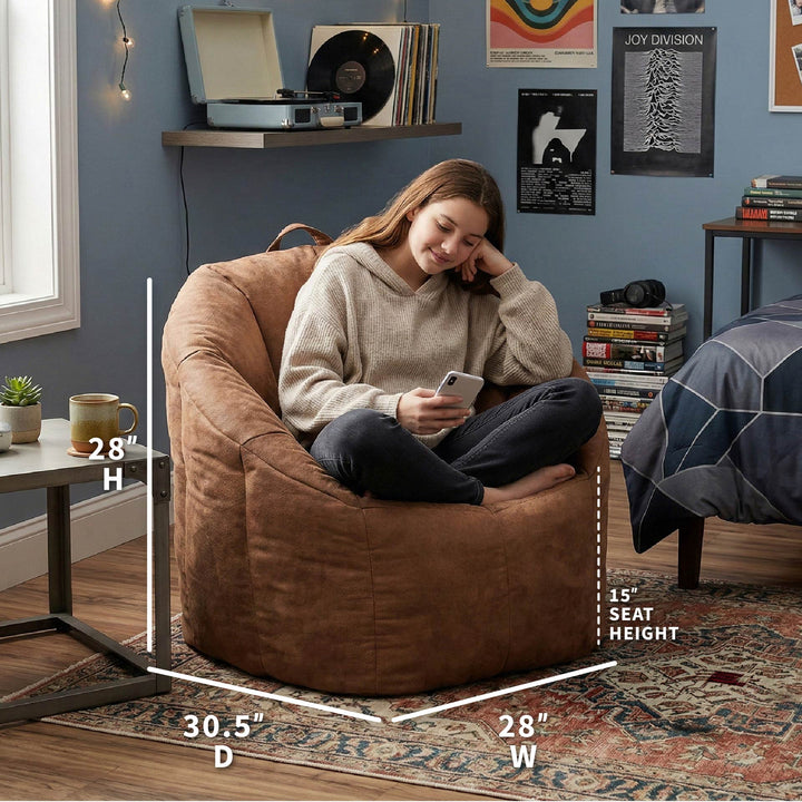Woman sitting on a brown bean bag chair in a room with shelves and decor. #color_chestnut-vegan-suede