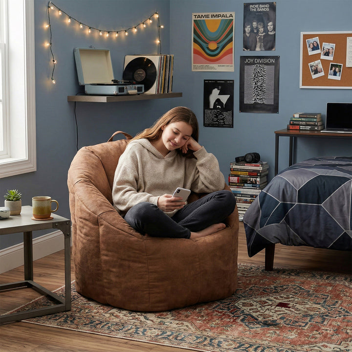 Woman sitting on a bean bag chair in a cozy room with posters and a record player. #color_chestnut-vegan-suede
