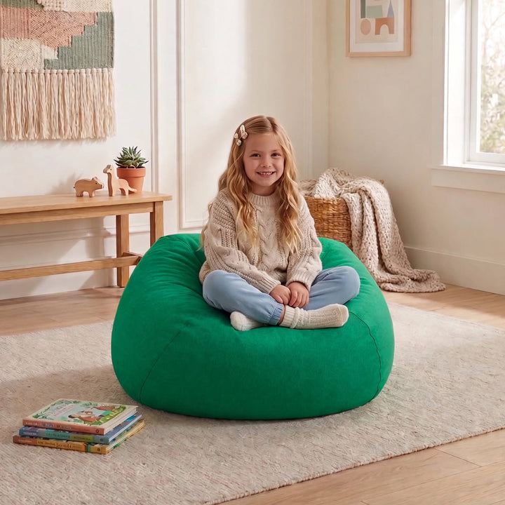 A young girl with blonde hair sits cross-legged on a large, round green bean bag chair in a bright, modern children&