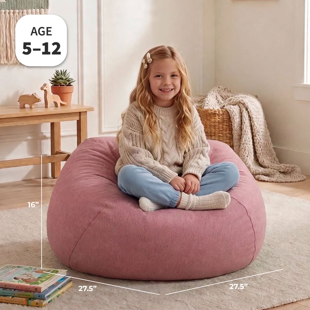 A young girl sits cross-legged on a large dusty pink bean bag chair in a cozy, sunlit room. White dimension lines and text overlays show the bean bag&