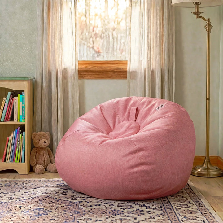 A dusty pink fabric bean bag chair placed on a patterned area rug in a child&