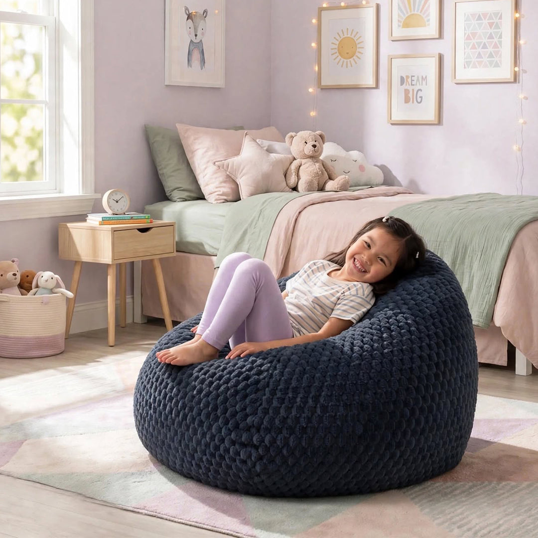 A young girl smiling while reclining on a large, dark navy blue textured bean bag chair in a child&