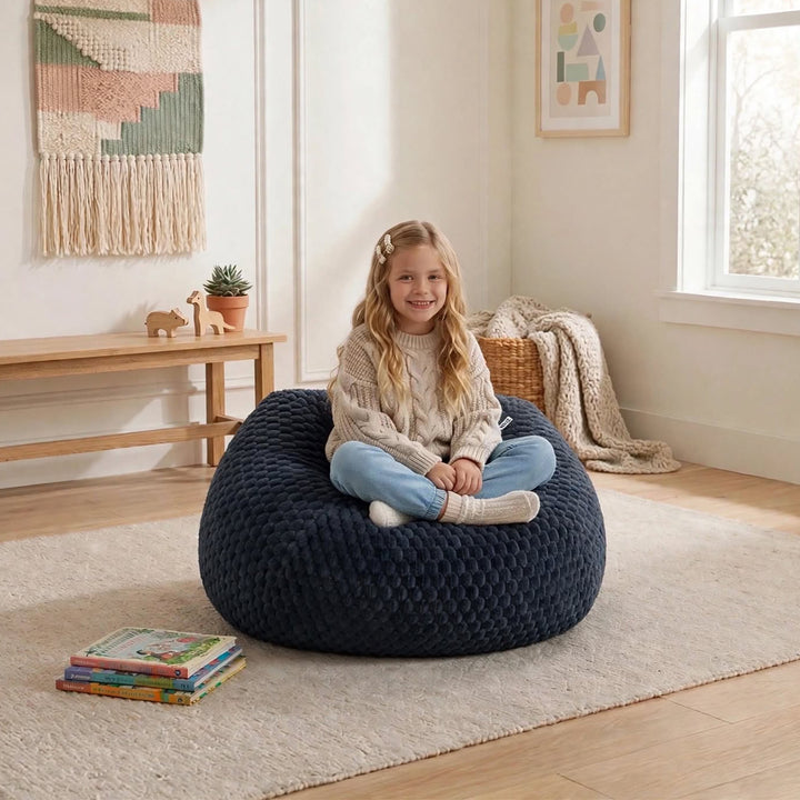 A young girl sits cross-legged on a large, dark navy blue textured bean bag chair in a bright, modern children&