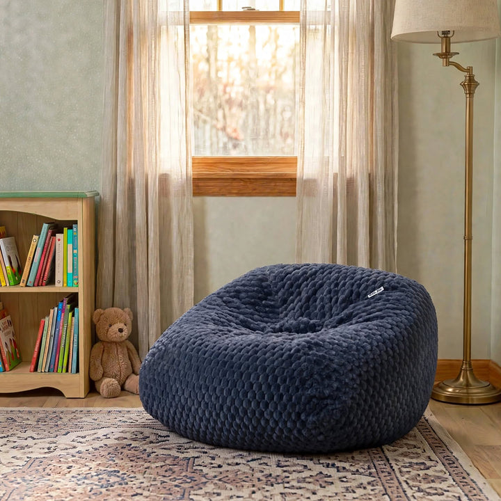 A large, plush navy blue bean bag chair with a textured, dimpled fabric surface, styled in a cozy child&