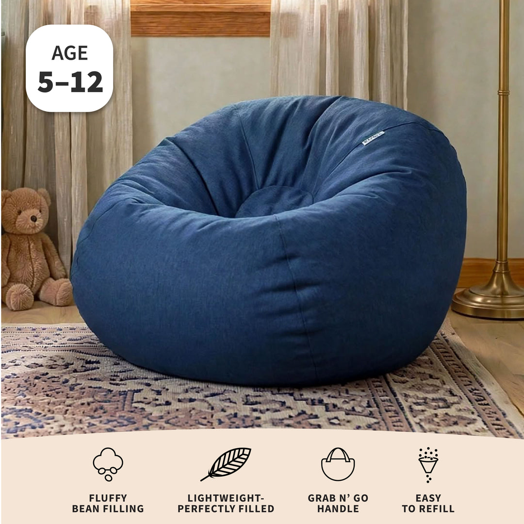 A large navy blue bean bag chair in a cozy room setting with a rug, teddy bear, and floor lamp, featuring an &