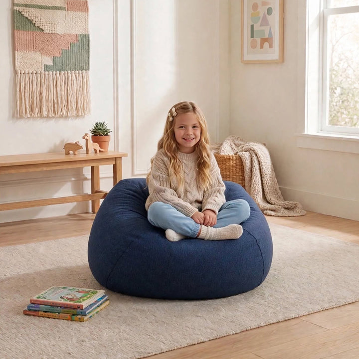 A young girl sits cross-legged on a large navy blue bean bag chair in a bright, modern child&